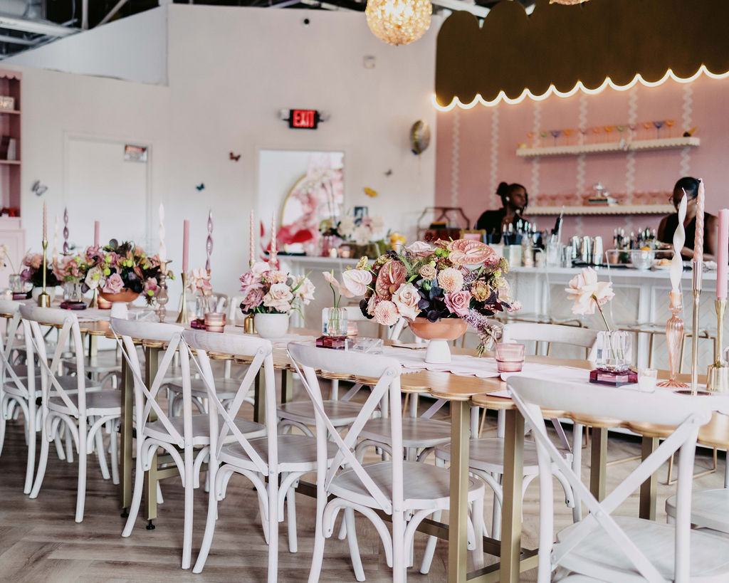 Elegant table setting with floral centerpieces and pink decor at the Aroma & Ambiance event by Indigo Pruitt Designs, with a stylish bar setup in the background.