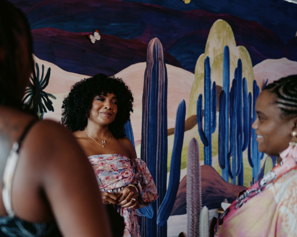 Marie Cloud engaging in conversation with guests against a colorful desert-themed mural at the Aroma & Ambiance event by Indigo Pruitt Designs